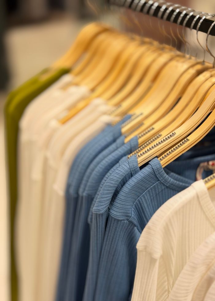 A row of neatly arranged colorful clothes on wooden hangers in a retail store setting.